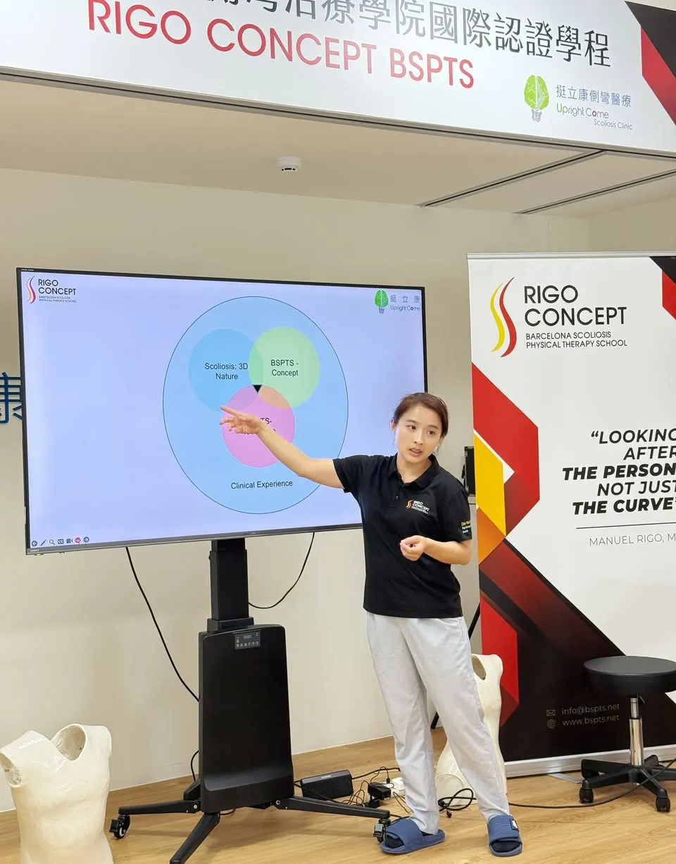 講師指著螢幕講解文氏圖：Scoliosis: 3D Nature、BSPTS-Concept、BSPTS-Technique 三圈位於 Clinical Experience 之內；後方為 Rigo Concept 展架