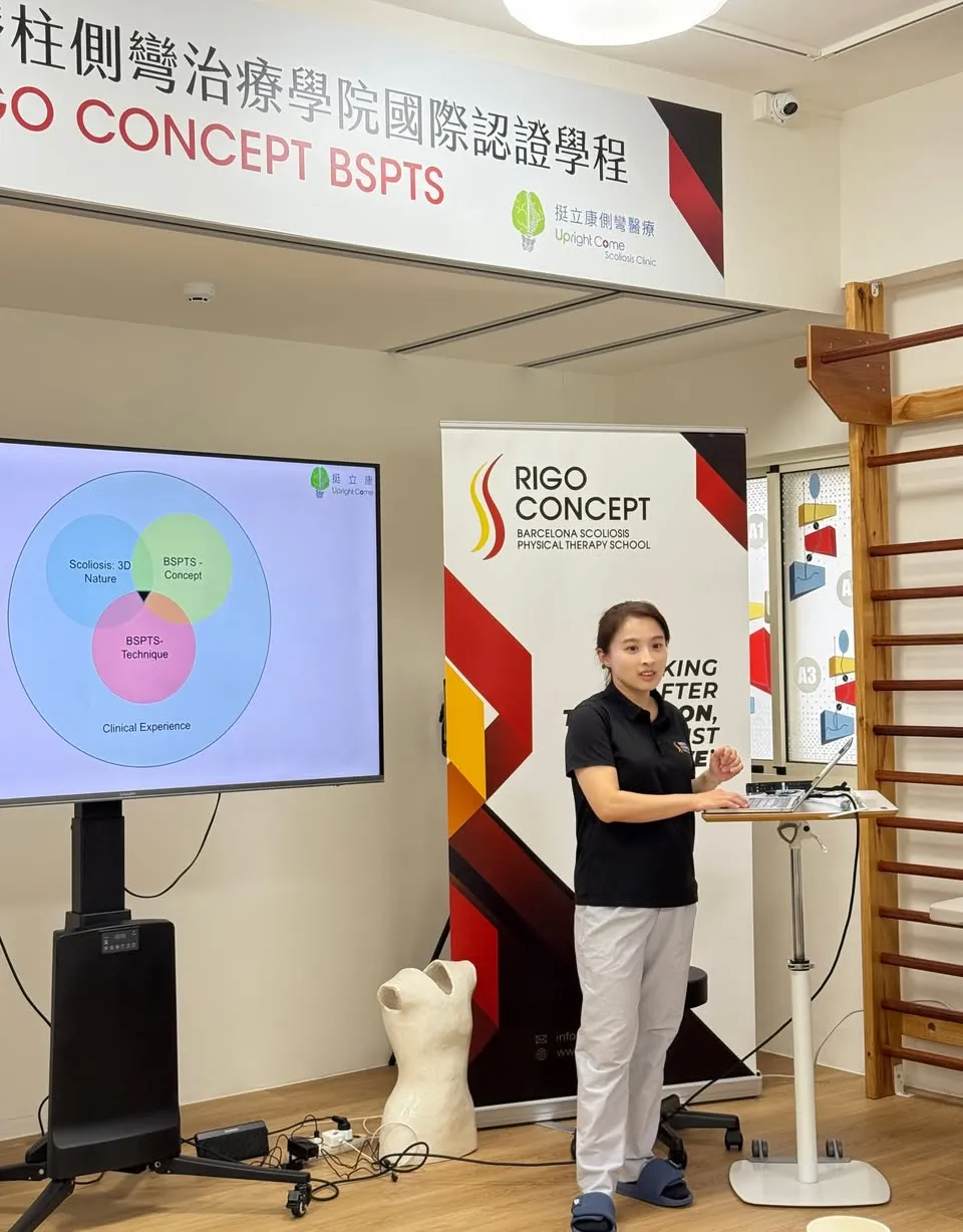 講師站在筆電講台旁授課，左側螢幕顯示 BSPTS 概念、技術與臨床經驗的文氏圖，上方橫幅寫著「脊柱側彎治療學院國際認證學程 RIGO CONCEPT BSPTS」